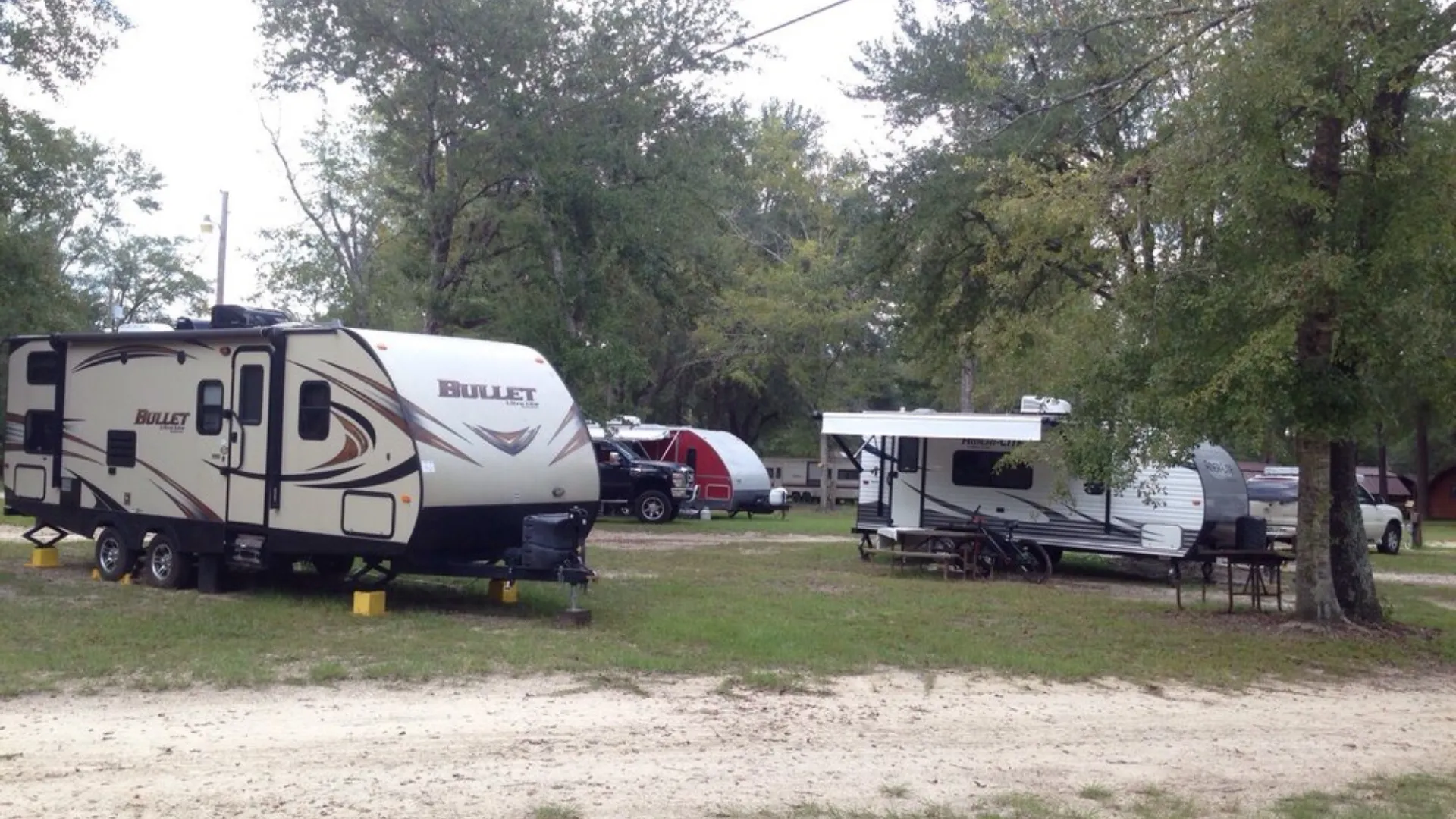 Several travel trailers, including a Bullet Ultra Lite, parked in level, grassy campsites with tree shade at an RV resort in Tallahassee.