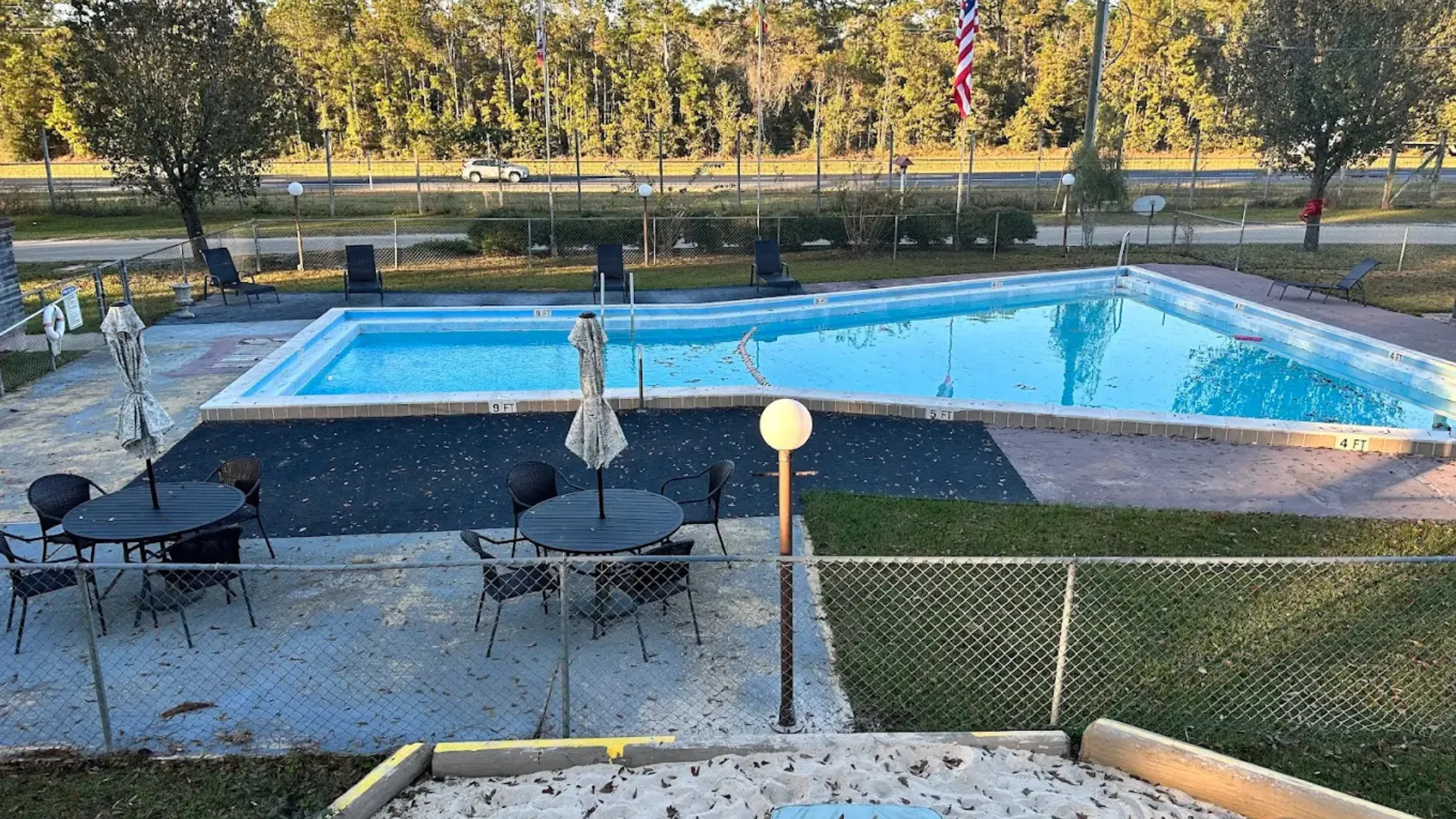 An outdoor swimming pool at a Tallahassee RV park with patio tables, umbrellas, and a sand volleyball court in the foreground.