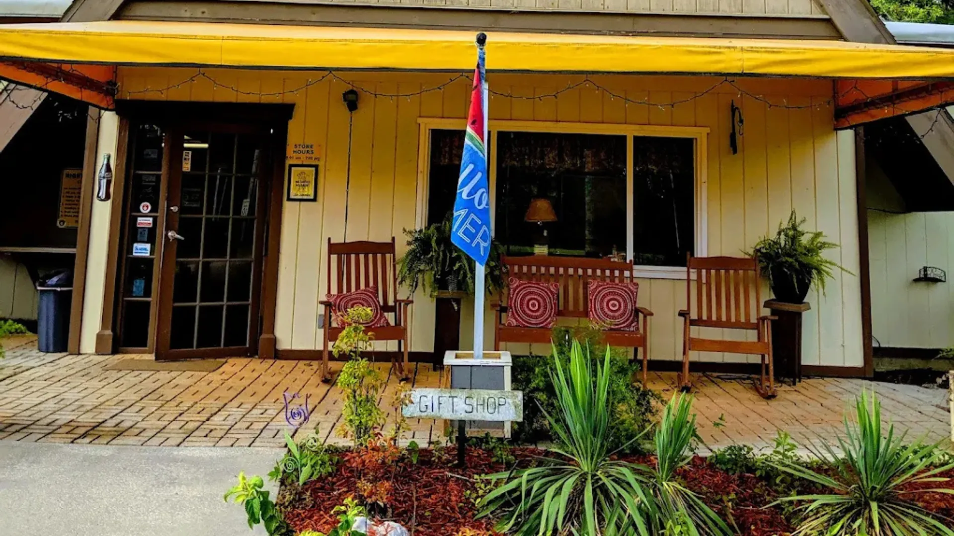 The entrance to the Tallahassee RV park gift shop featuring a yellow awning, wooden rocking chairs on a brick porch, and a "Gift Shop" sign.