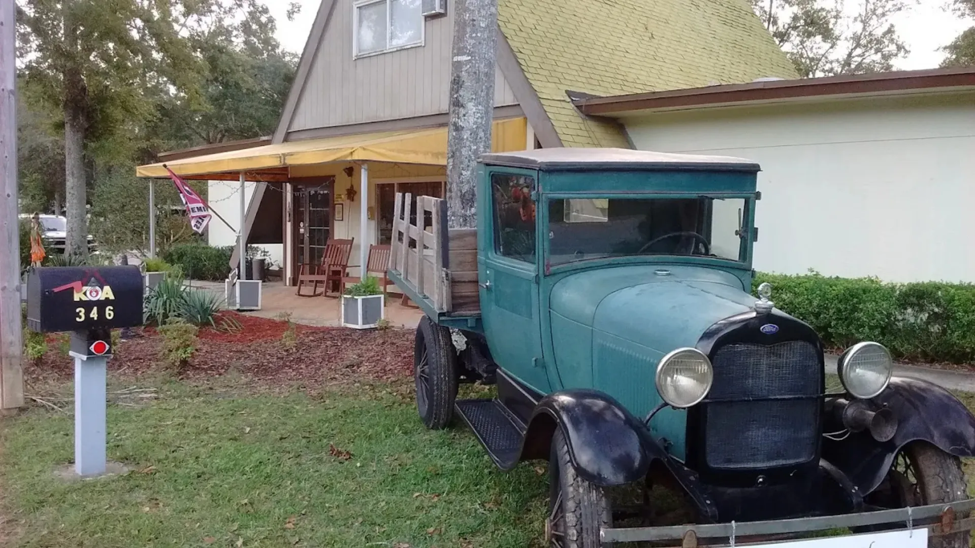 A vintage turquoise flatbed truck parked in front of the A-frame main office and check-in center of a Tallahassee RV park.