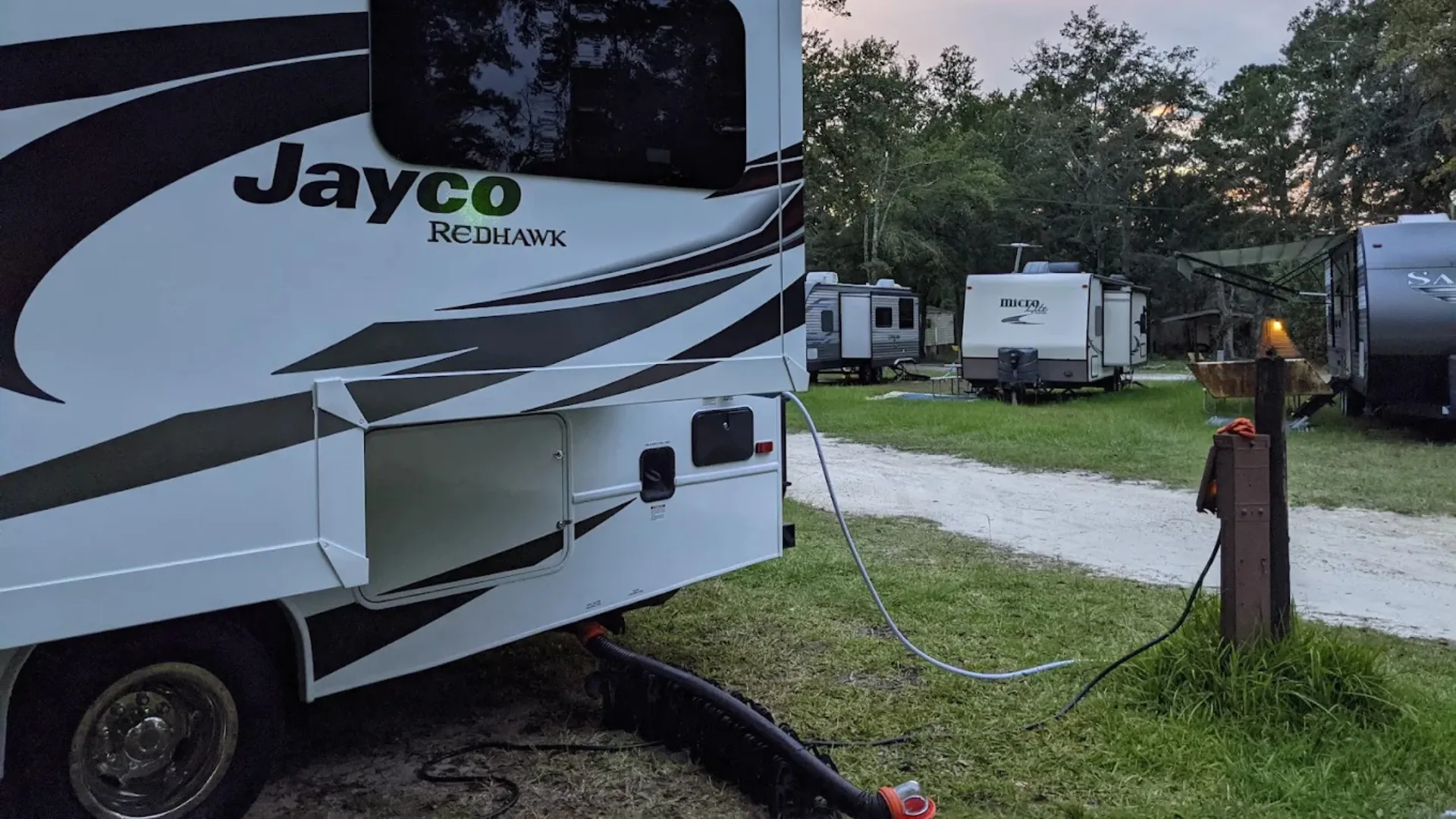 A Jayco Redhawk motorhome connected to water and sewer utilities at a full-hookup campsite in a Tallahassee RV resort.