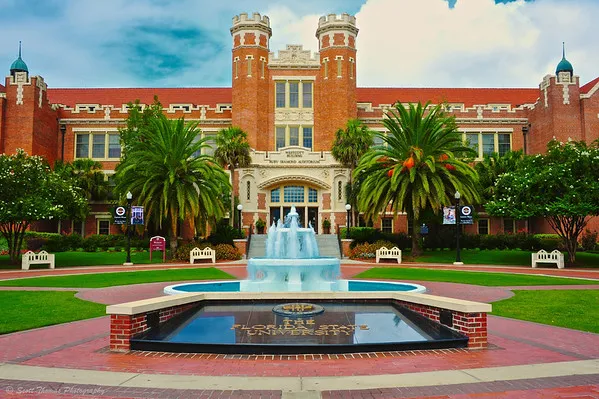 The historic brick Westcott Building at Florida State University featuring a large fountain, palm trees, and manicured green lawns under a cloudy sky.