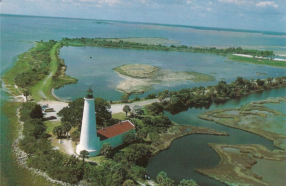 Aerial postcard view of the historic white St. Marks Lighthouse and keeper's quarters near Tallahassee, Florida, surrounded by coastal marshes and water.